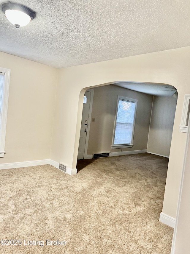 carpeted empty room with arched walkways, visible vents, a textured ceiling, and baseboards