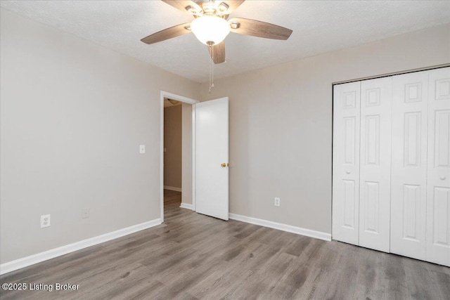 unfurnished bedroom featuring wood finished floors, baseboards, a closet, and a textured ceiling