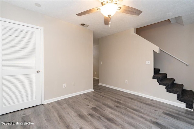 unfurnished living room featuring stairway, a ceiling fan, wood finished floors, visible vents, and baseboards