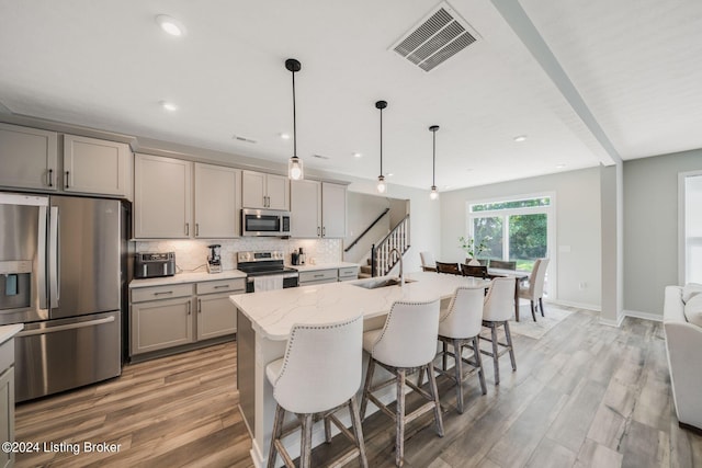 kitchen featuring visible vents, a breakfast bar, gray cabinetry, decorative backsplash, and stainless steel appliances