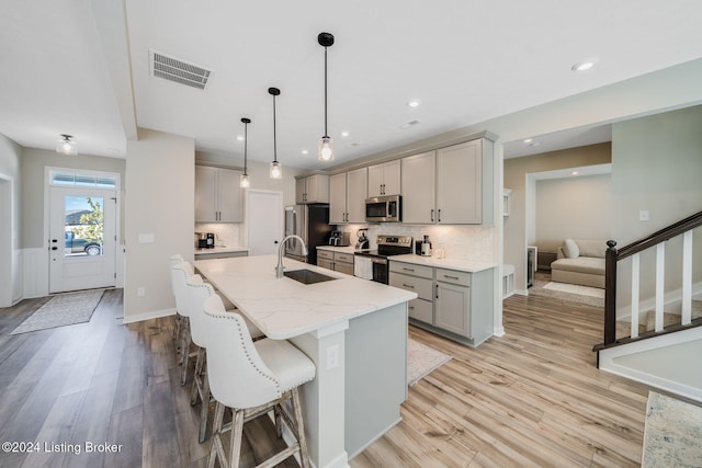 kitchen featuring visible vents, gray cabinetry, light wood-style flooring, stainless steel appliances, and a sink