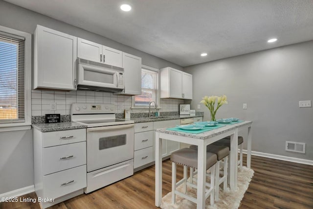 kitchen featuring visible vents, white appliances, dark wood-type flooring, and baseboards