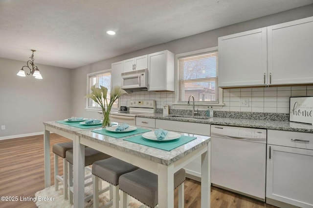 kitchen with white appliances, light wood finished floors, a sink, decorative backsplash, and a notable chandelier