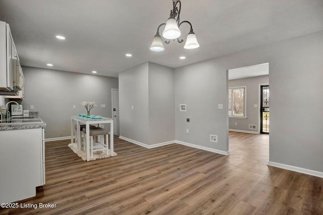 unfurnished dining area featuring baseboards, dark wood finished floors, recessed lighting, an inviting chandelier, and a sink