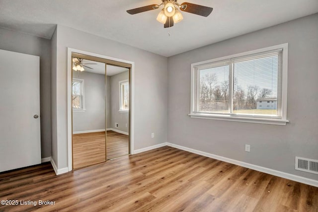 unfurnished bedroom featuring visible vents, ceiling fan, baseboards, wood finished floors, and a closet