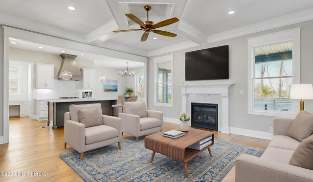living room with coffered ceiling, beam ceiling, light wood-style floors, crown molding, and ceiling fan with notable chandelier