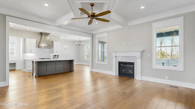 kitchen with a wealth of natural light, beamed ceiling, ceiling fan with notable chandelier, and light wood-style floors
