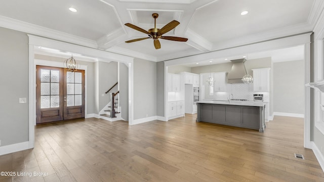 interior space featuring premium range hood, coffered ceiling, white cabinets, light wood-style floors, and ceiling fan with notable chandelier