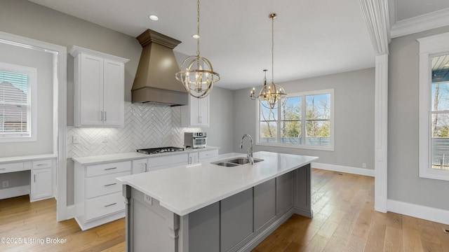 kitchen with tasteful backsplash, custom exhaust hood, a notable chandelier, gas stovetop, and a sink
