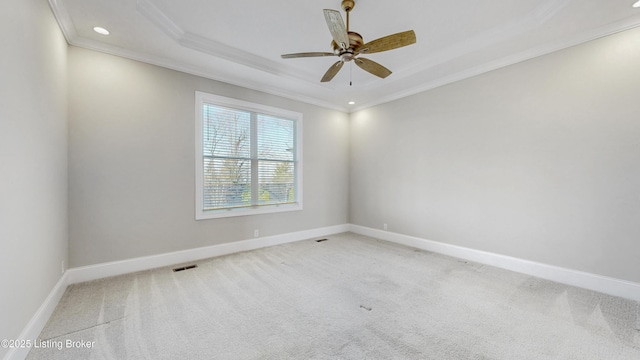 empty room featuring a raised ceiling, a ceiling fan, carpet floors, crown molding, and baseboards