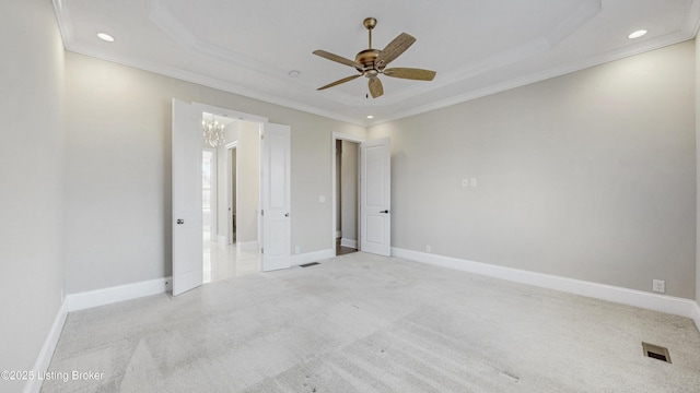 carpeted spare room with a raised ceiling, crown molding, and baseboards