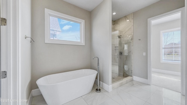 bathroom with a shower stall, a freestanding bath, and baseboards