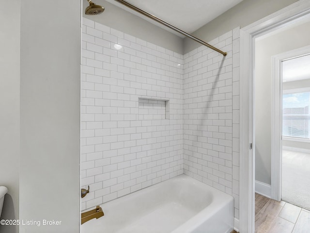 full bath featuring wood finished floors, washtub / shower combination, and baseboards