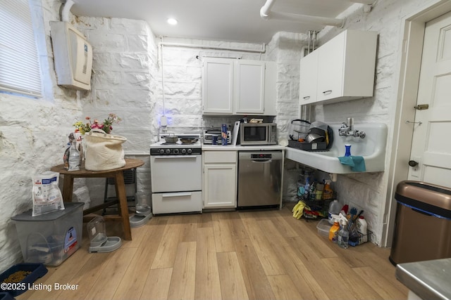kitchen with light wood-type flooring, light countertops, stainless steel appliances, white cabinetry, and a sink
