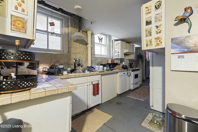 kitchen featuring concrete floors, tile counters, under cabinet range hood, white range with gas cooktop, and white cabinets