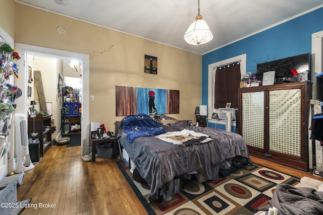 bedroom with wood-type flooring, a notable chandelier, and crown molding