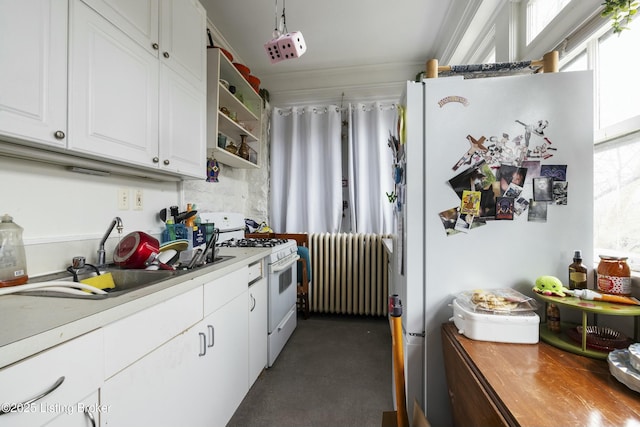 kitchen featuring a healthy amount of sunlight, radiator heating unit, white appliances, white cabinetry, and a sink