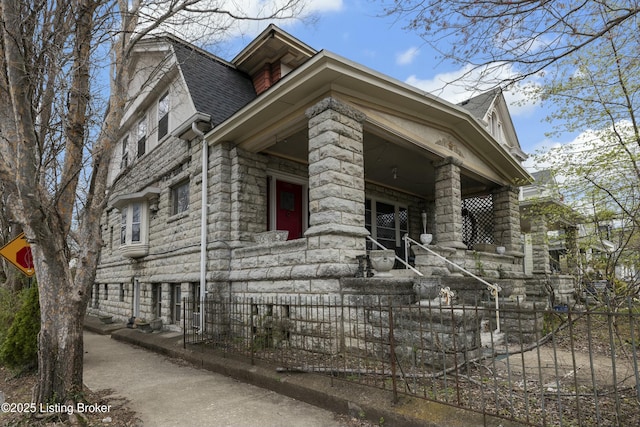 view of home's exterior featuring a porch, stone siding, and roof with shingles