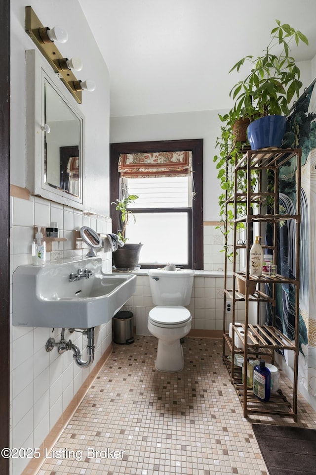 half bathroom featuring a wainscoted wall, toilet, a sink, tile walls, and tile patterned flooring