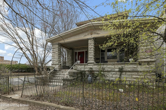 view of front of house with a fenced front yard, stone siding, and covered porch
