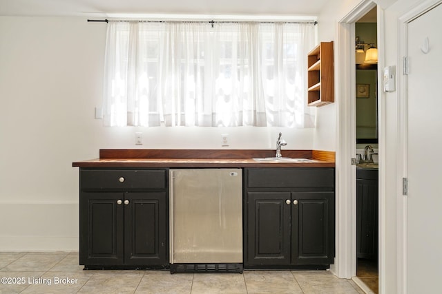 bar featuring light tile patterned floors, wet bar, refrigerator, a sink, and baseboards