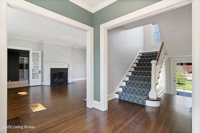 interior space featuring a fireplace with flush hearth, wood finished floors, baseboards, and ornamental molding