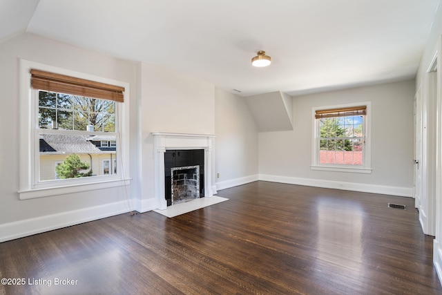 unfurnished living room with visible vents, baseboards, dark wood finished floors, vaulted ceiling, and a fireplace with flush hearth