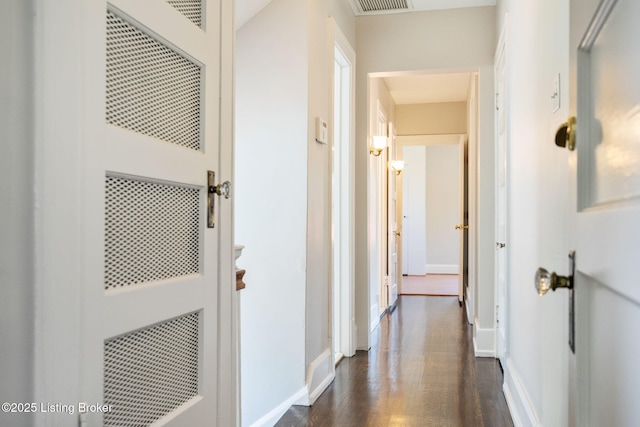 corridor featuring visible vents, a heating unit, baseboards, and dark wood finished floors