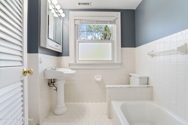 bathroom featuring a bath, tile walls, visible vents, and wainscoting
