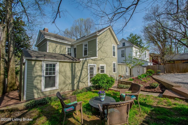 back of property with an outdoor structure, fence, a chimney, and a storage unit