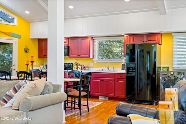 kitchen featuring beamed ceiling, black appliances, light wood-style flooring, a sink, and open floor plan