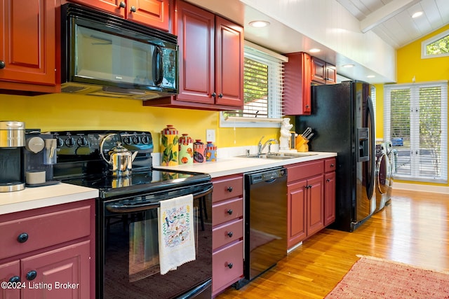 kitchen featuring vaulted ceiling with beams, washing machine and dryer, light wood-type flooring, black appliances, and a sink