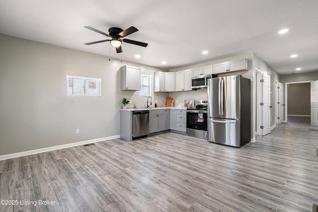 kitchen with a ceiling fan, stainless steel appliances, light wood-style floors, light countertops, and baseboards