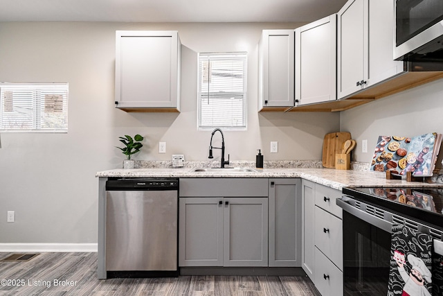 kitchen featuring gray cabinetry, light stone countertops, wood finished floors, stainless steel appliances, and a sink