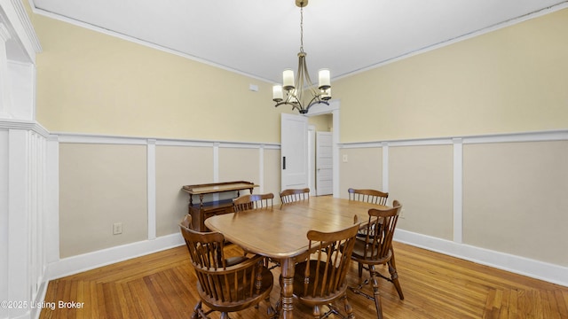 dining area with an inviting chandelier, a decorative wall, a wainscoted wall, and ornamental molding