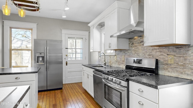 kitchen with a sink, dark countertops, stainless steel appliances, wall chimney exhaust hood, and decorative backsplash