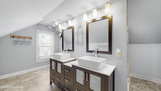 full bath with vaulted ceiling, two vanities, baseboards, and a sink
