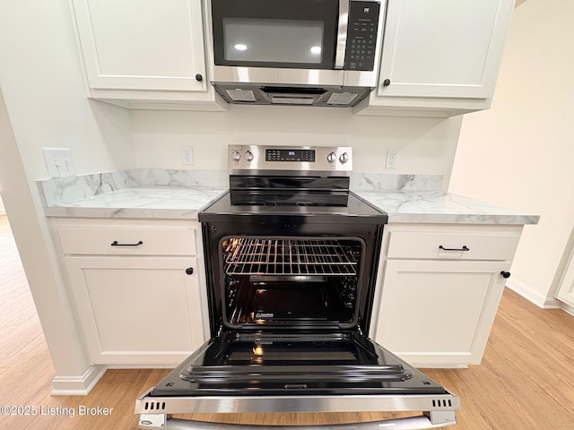 3833 Jupiter Rd, Louisville, KY 40218 - kitchen view of stainless steel microwave, light wood finished floors, electric stove, white cabinets, and baseboards