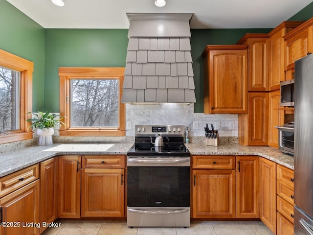 kitchen featuring a wealth of natural light, custom range hood, light stone counters, and appliances with stainless steel finishes