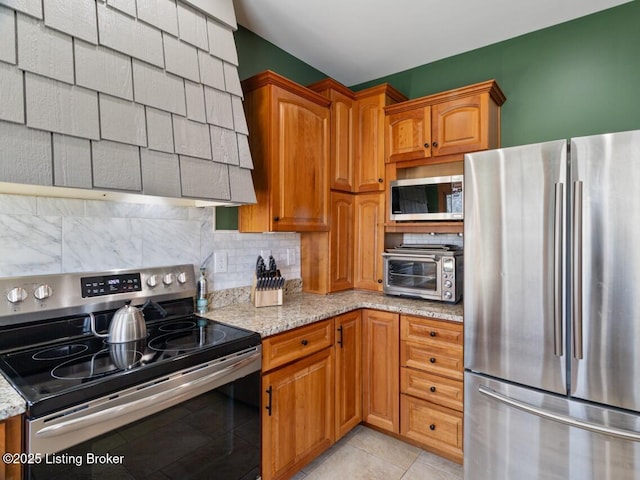 kitchen with decorative backsplash, a toaster, light stone countertops, brown cabinets, and appliances with stainless steel finishes