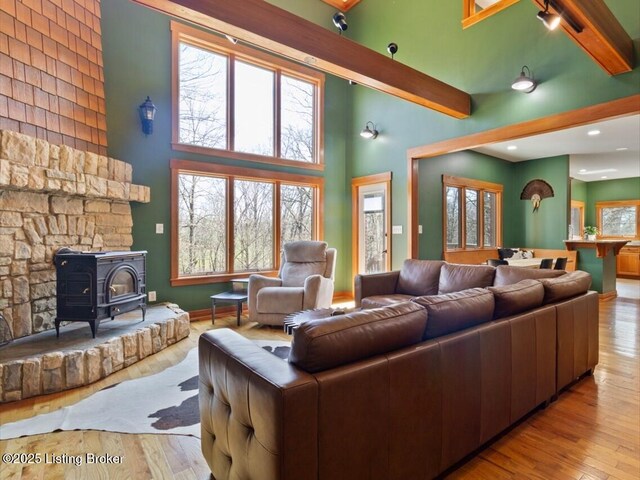 living area with a high ceiling, wood finished floors, beamed ceiling, and a wood stove