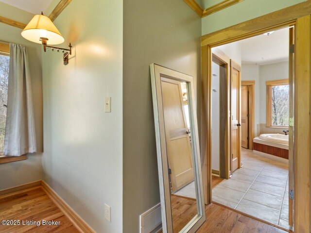 corridor with baseboards, light wood finished floors, and visible vents