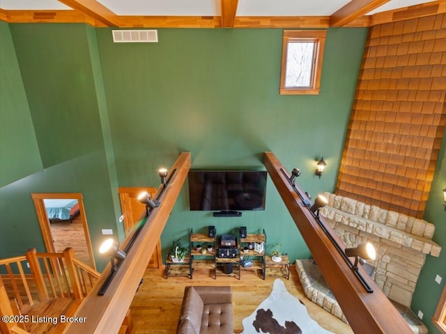 unfurnished living room featuring wood finished floors, stairway, beamed ceiling, and visible vents