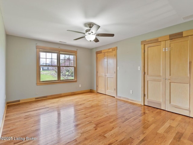 unfurnished bedroom with baseboards, ceiling fan, two closets, and light wood finished floors