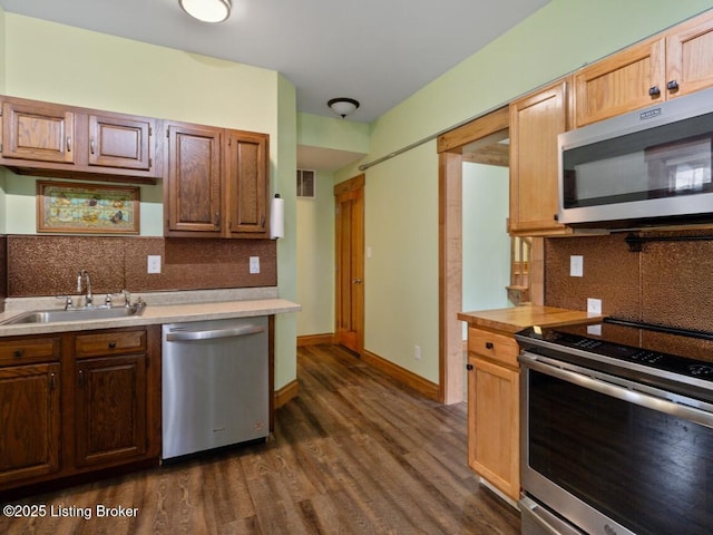 kitchen with light countertops, a sink, appliances with stainless steel finishes, and dark wood finished floors