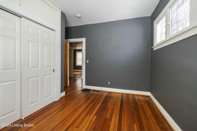 unfurnished bedroom featuring dark wood-style floors, a closet, and baseboards
