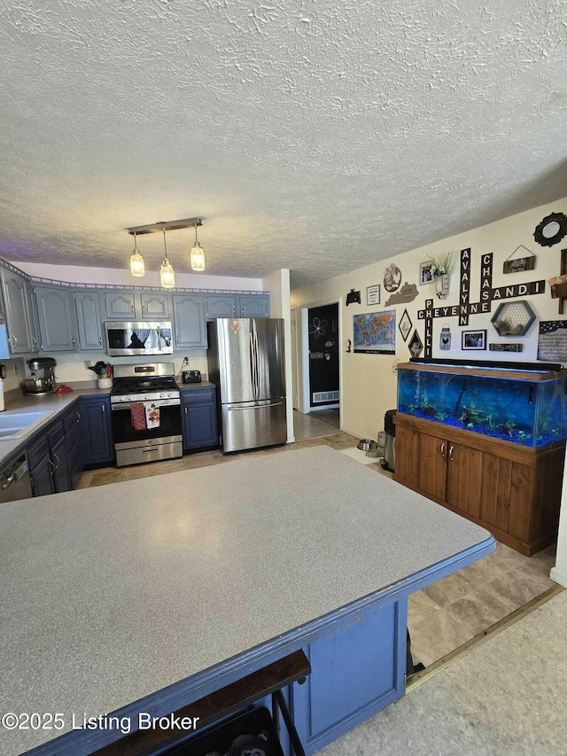 kitchen featuring blue cabinetry, a sink, a textured ceiling, stainless steel appliances, and hanging light fixtures