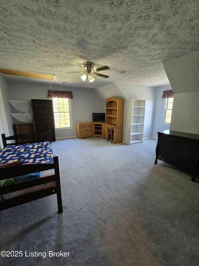 carpeted bedroom with multiple windows, a textured ceiling, attic access, and vaulted ceiling