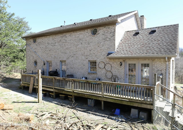 back of property with a deck, brick siding, roof with shingles, and a chimney