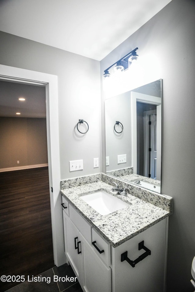 half bath with vanity, baseboards, and wood finished floors
